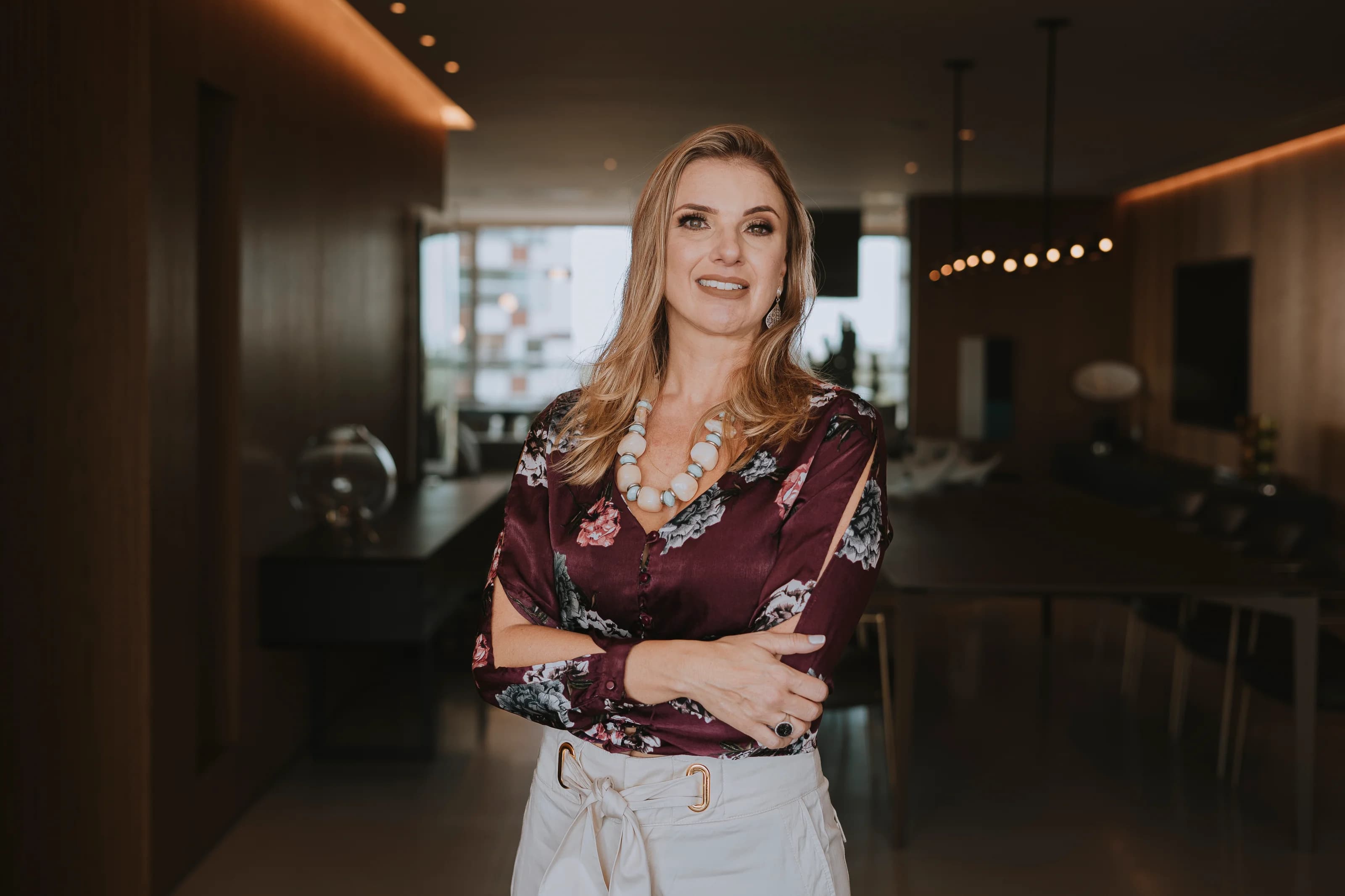 Ana Alarcon sorrindo em um living de madeira com iluminação quente